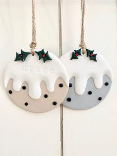 two ceramic christmas ornaments hanging from strings on a white wooden wall with black dots and holly decorations