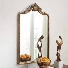 a bowl of oranges sitting on top of a table next to a large mirror