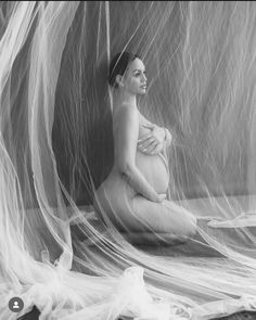 black and white photograph of a woman sitting on the floor with sheer fabric covering her body