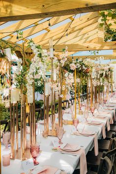 an outdoor dining area with tables and chairs covered in white tablecloths, gold vases filled with flowers and greenery