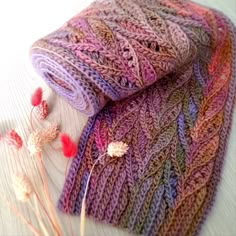 a knitted blanket sitting on top of a table next to dried flowers and leaves