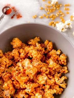 a white bowl filled with popcorn next to a spoon and corn kernels on the side