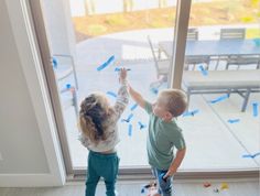 two young children are playing with blue streamers on the window sill in front of them