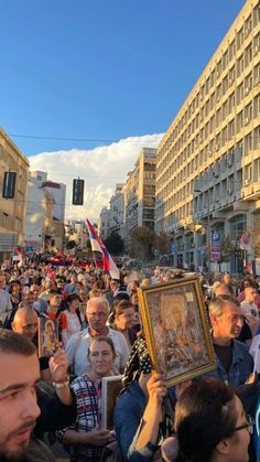 a large group of people standing in the middle of a street holding up framed pictures