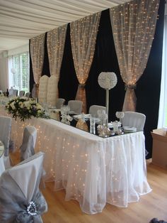 a table set up for a formal function with white chairs and lights on the walls