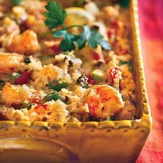 a casserole with shrimp and vegetables in it on a red table cloth next to a fork