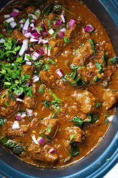 meat and vegetable stew in a crock pot with onions, cilantro and parsley