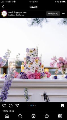 a wedding cake sitting on top of a table next to purple and pink flowers in vases