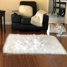 a living room with a black leather couch and white fur rug on the wooden floor