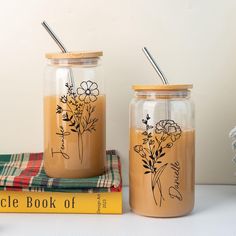 two mason jars with flowers on them sitting next to a stack of books and yarn