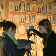 two women standing in front of a camera with an image on the wall behind them