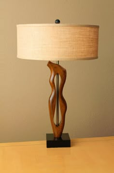 a wooden table lamp sitting on top of a wooden desk next to a white wall