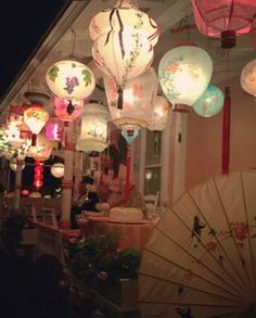 many lanterns are hanging from the ceiling above a woman holding an umbrella in front of her