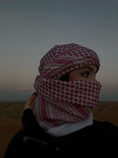 a woman wearing a red and white scarf covering her face in front of the sun