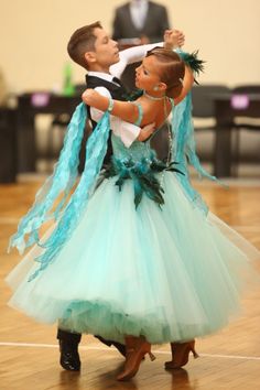 a man and woman dance on a wooden floor in formal attire with blue tulle skirts