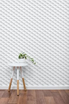 a white table with a potted plant on it in front of a textured wall