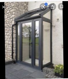 an open glass door on the side of a building next to a flower bed and potted plant