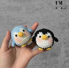 two small crocheted penguins sitting next to each other on a persons hand in front of a gray background