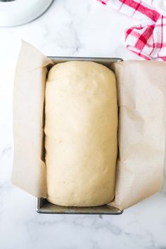 an uncooked loaf of bread in a box on a marble countertop next to a red and white checkered napkin