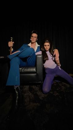 a man and woman sitting on a chair in front of a black curtain holding swords