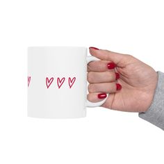 a woman's hand holding a white coffee mug with red hearts printed on it