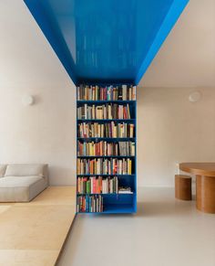 a blue book shelf filled with lots of books next to a white couch and table