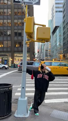 a woman is crossing the street in front of a traffic light and trash can on the side of the road