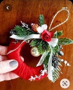 someone is holding a christmas ornament in their hand on a wooden table with white and red decorations