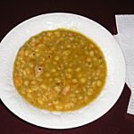 a white bowl filled with beans next to a spoon and napkin on a table top