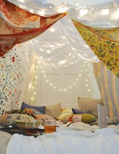 a bed covered in lots of pillows and blankets with lights on the ceiling above it