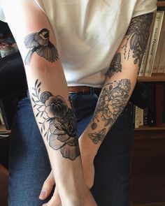 two people with tattoos on their arms holding each other's hands in front of a bookshelf