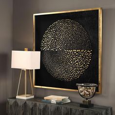 a black and gold painting on a wall next to a table with a white lamp