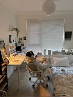 a bedroom with a bed, desk and computer on it in front of a window