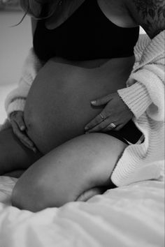 a pregnant woman sitting on top of a bed with her stomach exposed and hands under her belly