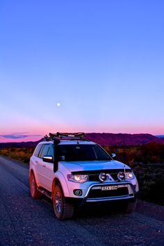 a white suv parked on the side of a road at dusk with mountains in the background