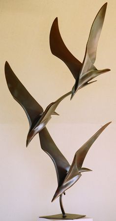 three metal birds flying in the air on top of a white pedestal with a black base