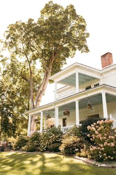 a large white house sitting on the side of a lush green field next to a tree