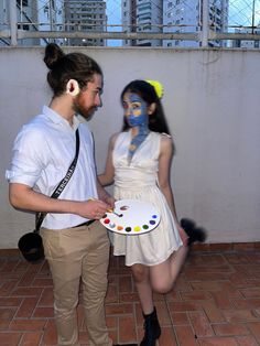 a man standing next to a woman holding a plate with paint on it and the girl has her face painted