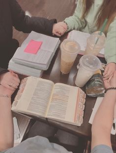 two people sitting at a table holding hands over an open book and drinking milkshakes