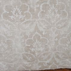 a white and beige wallpaper with an intricate design on it's side, next to a wooden floor