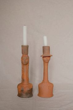 two candles are sitting next to each other on a white tablecloth covered surface, one has a candle holder and the other has a head