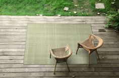 two wicker chairs sitting on top of a wooden deck next to a green rug