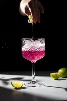 a person is squeezing a drink into a glass with ice and limes around it