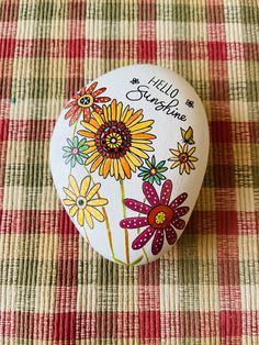 a button with flowers painted on it sitting on a plaid tablecloth covered surface in the shape of a heart