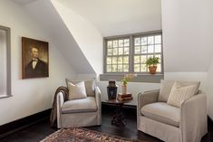 two chairs and a table in the corner of a room with a painting on the wall