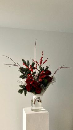 a vase filled with red flowers and greenery on top of a white block in a room