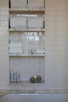 a bath tub sitting next to a shelf filled with toilet paper on top of it