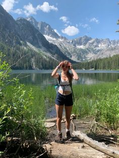 a woman standing on top of a log next to a lake with mountains in the background