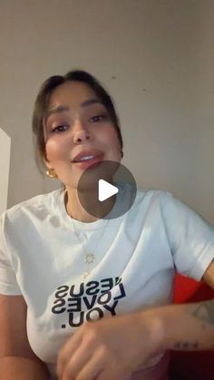 a woman sitting on top of a red couch in front of a white wall and wearing a t - shirt that says jesus loves you