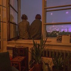 two people are sitting on a window sill looking out at the city below them